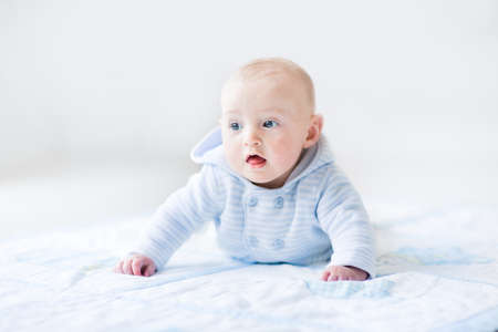 Funny baby boy playing on a blue blanket wearing a blue knitted sweater during tummy time in a sunny white room  の写真素材