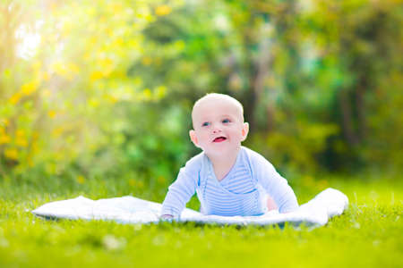 Adorable funny laughing baby boy in a blue shirt playing on his tummy relaxing on a white blanket in...