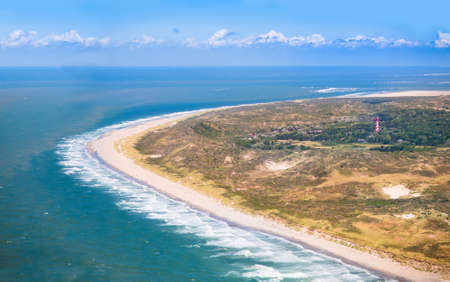 Aerial view of sand dunes and beach with a red and white lighthouse in Zeeland, Netherlands, taken from above on a helicopter tripの写真素材