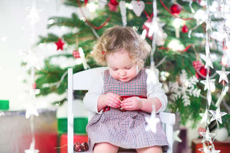 Cute toddler girl eating candy under a beautiful Christmas treeの写真素材