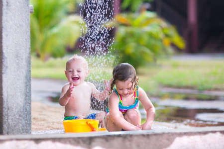 Two happy children, adorable baby boy and a little toddler girl in swimming suits playing in an outdoor shower in a tropical reaost during summer vacationの写真素材