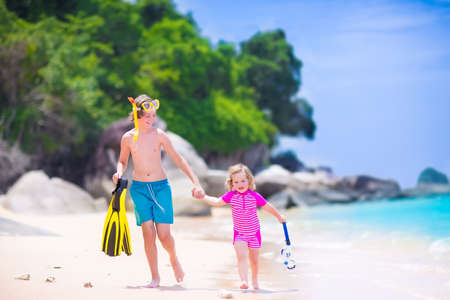 Two happy children, teenager boy and a little toddler girl, brother and sister, running on a beautiful tropical beach after snorkeling in the ocean having fun during summer vacationの写真素材