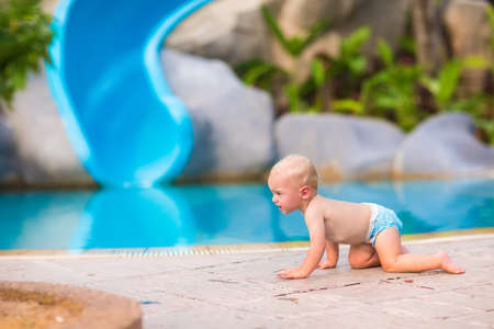 Cute little baby boy in a swimming diaper crawling at pool side having fun during summer vacation in a beautiful tropical resortの写真素材