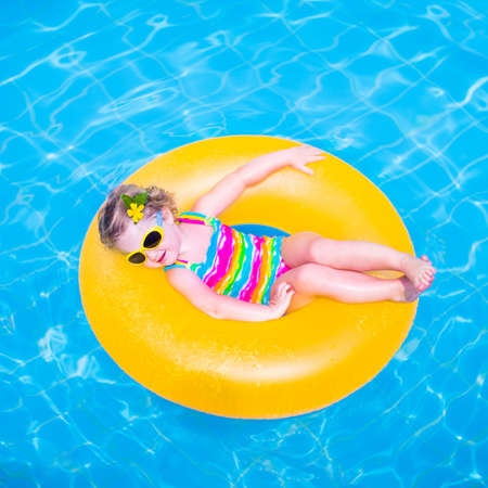 Cute funny little toddler girl in a colorful swimming suit and sun glasses relaxing on an inflatable...