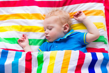 Child sleeping in colorful bed. Little baby boy asleep. Kids textile in rainbow color. Toddler kid relaxing on a sunny morning. Kids sleep at home.の写真素材