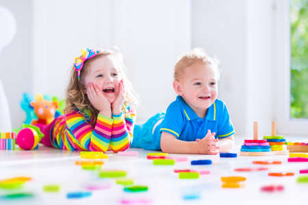 Kids playing with wooden toys. Two children, cute toddler girl and funny baby boy, playing with toy blocks, building towers at home or day care. Educational child toys for preschool and kindergarten. Kids playing with wooden toys. Two children, cute toddler girl and funny baby boy, playing with toy blocks, building towers at home or day care. Educational child toys for preschool and kindergarten.