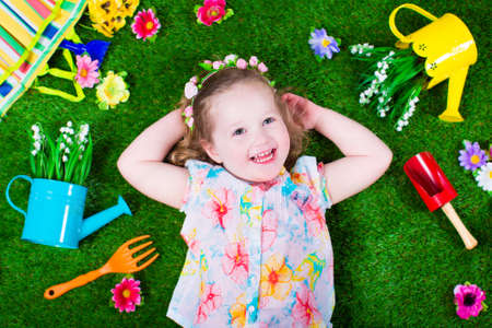 Kids gardening. Children with garden tools. Child with watering can and shovel. Little kid watering flowers. Girl relaxing on green backyard lawn in summer.の写真素材