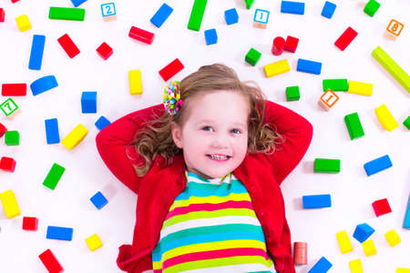 Child playing with colorful wooden toys. Little girl with educational toy blocks. Children play at day care or preschool. Mess in kids room. View from above.の写真素材