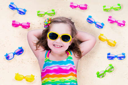 Child wearing sunglasses on a beach. Sun eye wear for kids. Little girl choosing spectacles. Lens and colorful frame choice for children. UV protection for kids. Safe glasses for tropical vacation.の写真素材