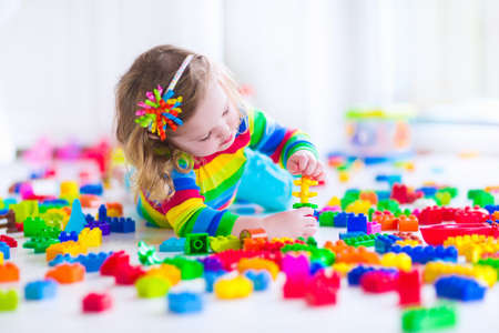 Preschooler child playing with colorful toy blocks. Kids play with educational toys at kindergarten or day care. Preschool children build tower with plastic block. Toddler kid in nursery.