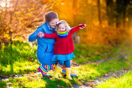 Mother and daughter play in autumn park. Parent and child walk in the forest on a sunny fall day....
