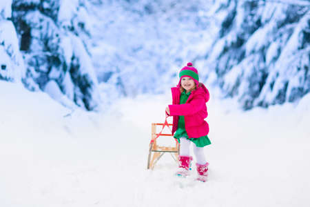 Little girl enjoying a sleigh ride. Child sledding. Toddler kid riding a sledge. Children play outdoors in snow. Kids sled in the Alps mountains in winter. Outdoor fun for family Christmas vacation.の写真素材