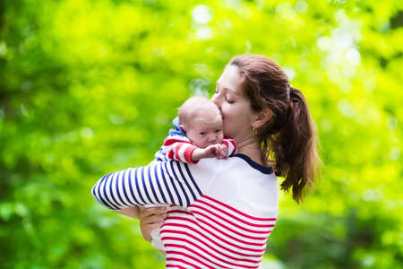 Mother holding newborn baby in a park. Mom playing with her new born son in the garden. Family with kids play outdoors. Young woman hugging little boy. Parents and children having fun in summer.の写真素材