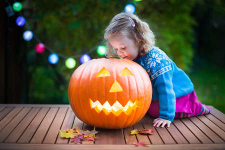 Little girl carving pumpkin at Halloween. Dressed up child trick or treating. Kids trick or treat. Child in witch costume playing in autumn park. Toddler kid with jack-o-lantern.の写真素材