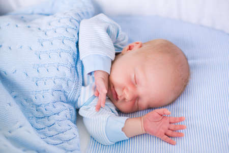 Newborn baby boy in bed. New born child sleeping under a blue knitted blanket. Children sleep. Bedding for kids. Infant napping in bed. Healthy little kid shortly after birth. Cable knit textile.の写真素材