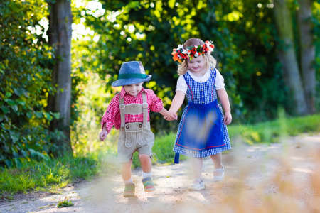 Kids in traditional Bavarian costumes in wheat field. German children eating bread and pretzel during Oktoberfest in Munich. Brother and sister play outdoors during autumn harvest time in Germany.の写真素材