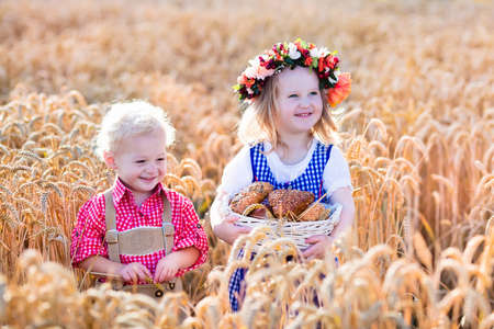 Kids in traditional Bavarian costumes in wheat field. German children eating bread and pretzel during Oktoberfest in Munich. Brother and sister play outdoors during autumn harvest time in Germany.の写真素材