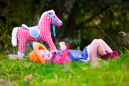 Little girl dressed up as cowgirl playing with toy rocking horse in park. Kids play cowboy outdoors. Children in Halloween costumes at trick or treat. Toys for preschooler kid or toddler child.の写真素材