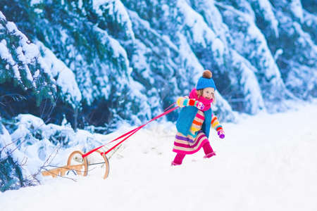 Little girl enjoying a sleigh ride. Child sledding. Toddler kid riding a sledge. Children play outdoors in snow. Kids sled in the Alps mountains in winter. Outdoor fun for family Christmas vacation.の写真素材