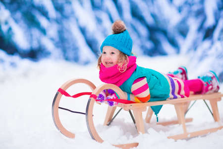 Little girl enjoying a sleigh ride. Child sledding. Toddler kid riding a sledge. Children play outdoors in snow. Kids sled in the Alps mountains in winter. Outdoor fun for family Christmas vacation.の写真素材
