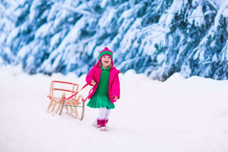 Little girl enjoying a sleigh ride. Child sledding. Toddler kid riding a sledge. Children play outdoors in snow. Kids sled in the Alps mountains in winter. Outdoor fun for family Christmas vacation.の写真素材