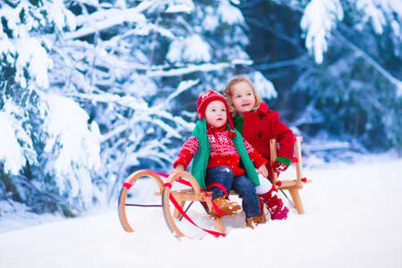 Little girl and boy enjoy a sleigh ride. Child sledding. Toddler kid riding a sledge. Children play outdoors in snow. Kids sled in Alps mountains in winter. Outdoor fun for family Christmas vacation.の写真素材