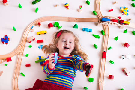 Child playing with wooden train, rails and cars. Toy railroad for kids. Educational toys for preschool and kindergarten children. Little girl at daycare. View from above, kid playing on the floor.の写真素材
