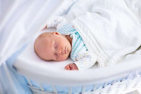 Newborn baby boy in bed. New born child sleeping under a white knitted blanket. Children sleep. Bedding for kids. Infant napping in bed. Healthy little kid shortly after birth. Cable knit textile.の写真素材