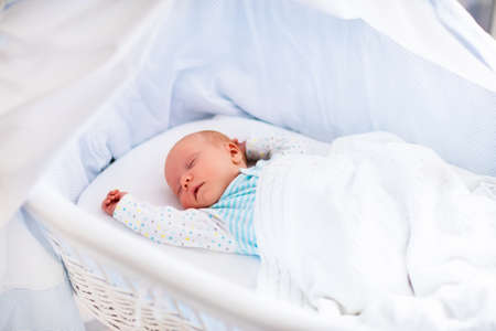 Newborn baby boy in bed. New born child sleeping under a white knitted blanket. Children sleep. Bedding for kids. Infant napping in bed. Healthy little kid shortly after birth. Cable knit textile.の写真素材