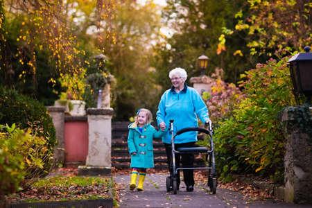 Happy senior lady with a walker or wheel chair and children. Grandmother and kids enjoying a walk in the park. Child supporting disabled grandparent. Family visit. Generations love and relationship.の写真素材