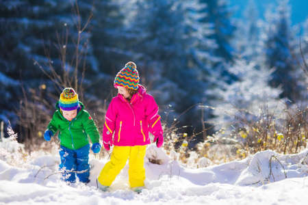 Children play in snowy forest. Toddler kids outdoors in winter. Friends playing in snow. Christmas vacation for family with young children. Little girl and boy in colorful jacket and knitted hat.の写真素材