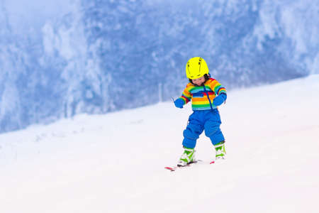 Child skiing in the mountains. Toddler kid in colorful suit and safety helmet learning to ski. Winter sport for family with young children. Kids ski lesson in alpine school. Snow fun for little skier.の写真素材