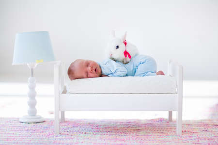 Adorable new born kid sleeping in a white toy bed with real rabbit. Nursery for newborn baby. Cute boy taking a nap in sunny bedroom with his bunny. Family with children and pets. Child and animal.の写真素材