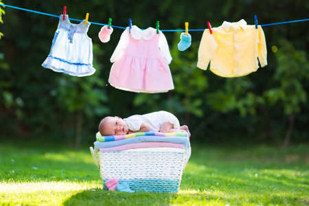 Newborn baby on a pile of clean dry towels. New born child after bath in a towel. Family washing clothes. Kids wear hanging on a line outdoors in summer garden. Infant apparel, textile for children.の写真素材