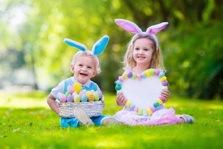Little boy and girl having fun on Easter egg hunt. Kids in bunny ears and rabbit costume. Children...