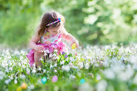 Little girl having fun on Easter egg hunt. Kids in blooming spring garden with crocus and snowdrop flowers. Children searching for eggs in the garden. Child putting colorful pastel eggs in a basket. Little girl having fun on Easter egg hunt. Kids in blooming spring garden with crocus and snowdrop flowers. Children searching for eggs in the garden. Child putting colorful pastel eggs in a basket.