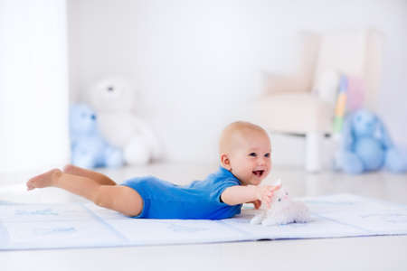 Adorable baby boy in white sunny bedroom. Newborn child relaxing on a rug. Nursery for young children. Furniture, textile and bedding for kids. New born kid during tummy time with toys at a window.の写真素材