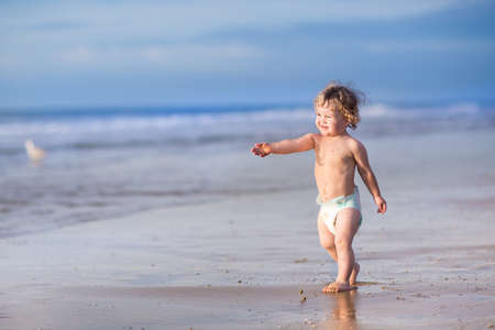 Funny little baby girl running on a beautiful tropical beach on a sunny warm summer eveningの写真素材