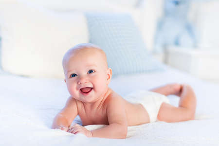 Baby boy wearing diaper in white sunny bedroom. Newborn child relaxing in bed. Nursery for children....