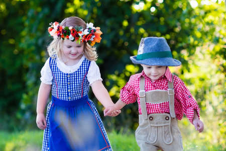 Kids in traditional Bavarian costumes in wheat field. German children eating bread and pretzel during Oktoberfest in Munich. Brother and sister play outdoors during autumn harvest time in Germany.の写真素材