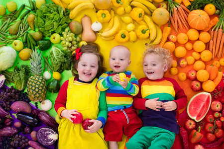 Boy, girl and baby with variety of fruit and vegetable. Colorful rainbow of raw fruits and...