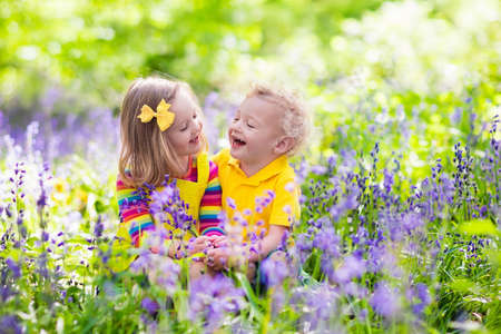 Kids gardening. Children play outdoors in bluebells meadow. Little girl and boy, brother and sister, work in the garden, planting bluebell flowers, watering blue bell flower bed. Family fun in summer.の写真素材