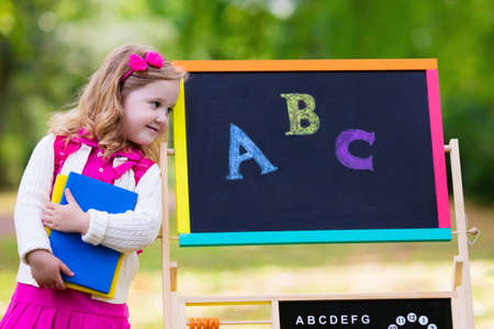 Child happy to be back to school. Funny little preschooler girl with backpack and books at black...