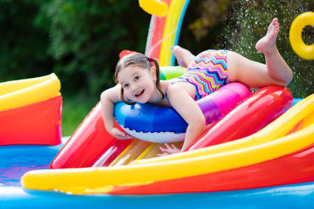 Children playing in inflatable baby pool. Kids swim and splash in colorful garden play center. Happy little girl playing with water toys on hot summer day. Family having fun outdoors in the backyard.の写真素材