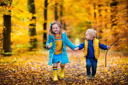 Happy children playing in beautiful autumn park on cold sunny fall day. Kids in warm jackets play with golden  leaves.の写真素材