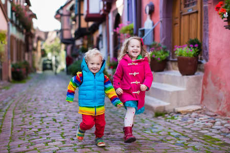 Cute little girl and boy walking down a street in historical medieval city center on cold autumn day. Children during fall vacation in Eguisheim, Alsace, France. Travelling and tourism with kids.の写真素材