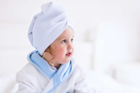 Child after bath. Cute little girl with wet curly hair wearing a bathrobe and head towel sitting on...