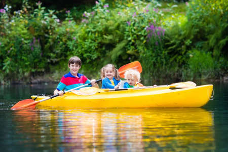 Happy family with three kids enjoying kayak ride on beautiful river. Little girl, toddler boy and teenager kayaking on hot summer day. Water sport and camping fun. Canoe and boat for children.の写真素材