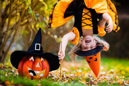 Little girl in witch costume playing in autumn park. Child having fun at Halloween trick or treat. Kids trick or treating. Toddler kid with jack-o-lantern. Children with candy bucket in fall forest.の写真素材