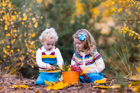 Happy children playing in beautiful autumn park on warm sunny fall day. Kids play with golden maple leaves.の写真素材